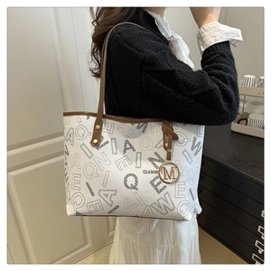 Close-up of the printed tote bag showing letter patterns and the metallic M pendant