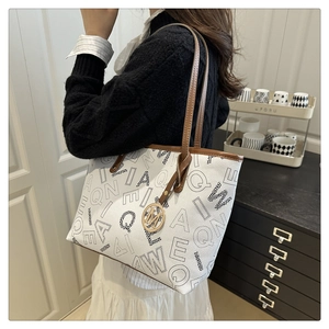 Detail of printed tote bag featuring brown leather straps and a gold M charm pendant