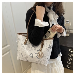 Detail of printed tote bag featuring brown handles and golden 'M' metal charm pendant