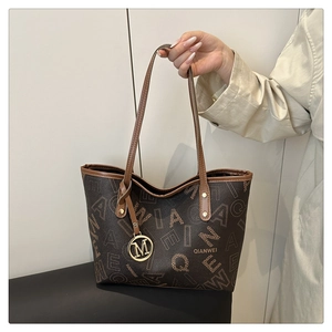 Detail of printed tote bag featuring brown leather, letter patterns and metal M pendant