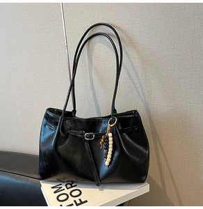 Dettaglio borsa a spalla in pelle nera con texture fine e ciondolo retrò in perline di legno