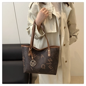 Detailed view of brown printed tote bag with leather handles and gold metal M charm