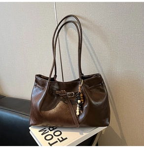 Dettaglio macro della borsa tote in pelle opaca marrone scuro con fibbia in metallo e ciondolo