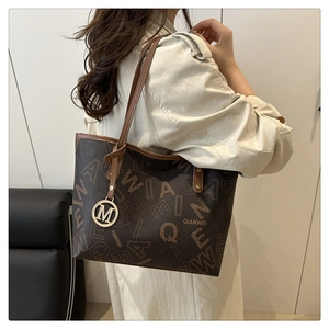 Macro detail of the brown tote bag featuring letter print and golden M pendant