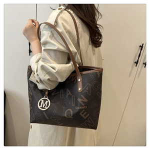 Detailed view of brown tote bag with logo print and metallic M charm on the shoulder strap