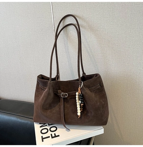Dettaglio borsa tote in pelle scamosciata marrone scuro con ciondolo di perline e fibbia