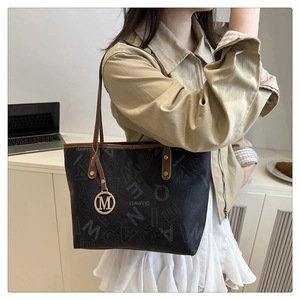 Close-up of the stylish printed tote bag featuring brown leather straps and golden M charm