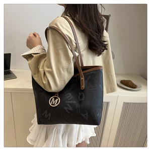 Close-up of printed tote bag with leather straps and a gold M-letter charm detail