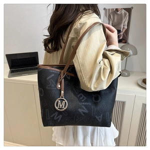 Close-up of a printed tote bag featuring a gold M-pendant and brown leather handles