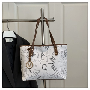 Detail of printed tote bag with brown leather handles and golden M charm pendant