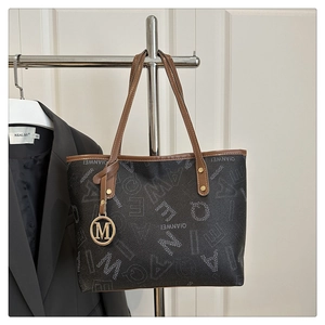 Close-up of printed tote bag with M-logo gold pendant and brown leather handle strap