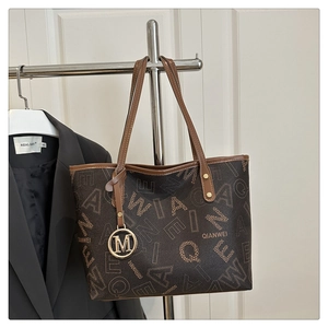 Detail of a brown printed tote bag featuring a golden M pendant and chic urban pattern