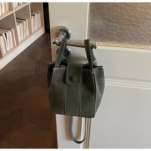 Detail of dark green bucket bag with white contrast stitching and magnetic closure