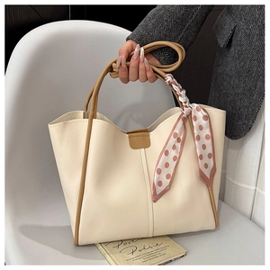 Detail of beige tote bag with brown contrast straps and decorative silk scarf accessory