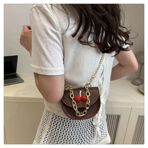 Close-up of brown leather bag with cherry ornament and gold chain handle on model
