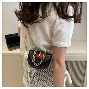 Detail of a black leather mini bag featuring 3D red cherry accents and a gold chain strap