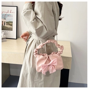 Detailed view of pink ruched handbag with bow accent and chain strap worn with white dress