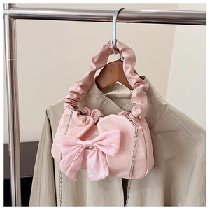 Detail of light pink ruched handbag featuring a large satin bow and golden chain strap