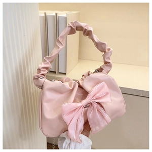 Detail of pink pleated handbag with a large bow and chain strap in a cozy setting