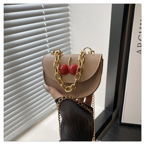 Dettaglio borsa a sella beige con motivo a ciliegia rossa e catena dorata decorativa