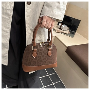 Detail of a brown leopard print shell bag featuring glossy leather trim and gold zippers