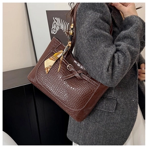 Detail of dark brown crocodile texture handbag with decorative floral scarf on the handle