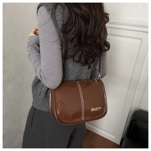 Detail of brown leather shoulder bag with white stitching and gold brand logo