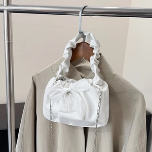 Elegant white ruched handbag with bow detail and silver chain on khaki trench background
