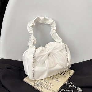 White pleated handbag with large lace bow and silver chain strap on vintage books