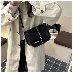 Detail of black crossbody bag with white contrast stitching and golden logo on model
