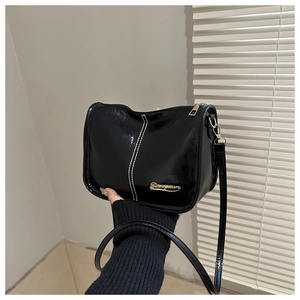 Détail d'un sac bandoulière en cuir verni noir avec surpiqûres blanches et logo doré
