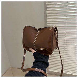 Détail d'un sac cabas en cuir marron brillant avec surpiqûres blanches et plaque dorée