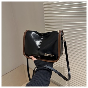 Détail du sac bandoulière en cuir verni noir avec garniture marron et logo doré