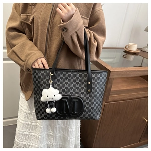 Detail of black tote bag with M-pattern print and a white cloud plush charm detail