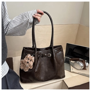 Detail of dark brown leather tote with decorative buckle and plush puppy charm