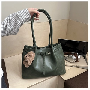 Detailed view of an olive green tote bag with knotted strap and a plush bear pendant