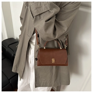 Detail of a dark brown leather crossbody bag with a gold buckle worn with a trench coat