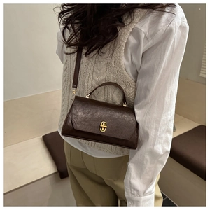 Detail of vintage brown leather handbag with gold rotating lock worn by a model