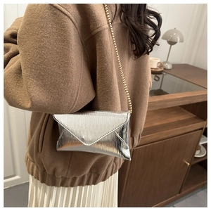 Detail of silver envelope crossbody bag with wave embossing and gold chain strap