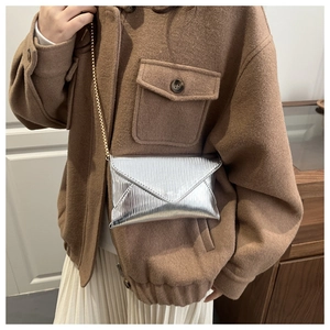 Detail of silver metallic envelope crossbody bag with gold chain strap and vertical texture