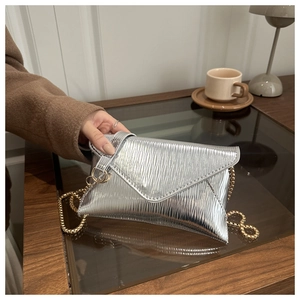 Detail of silver envelope clutch featuring pleated metallic texture and gold chain strap