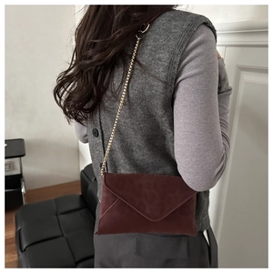 Dettaglio della borsa a busta bordeaux in pelle opaca con elegante catena dorata