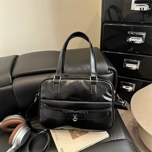 Large black shiny leather tote bag with bow and heart charm on a lifestyle background
