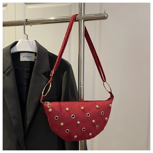Detail of red suede crescent bag with gold punk studs hanging on a modern display rack