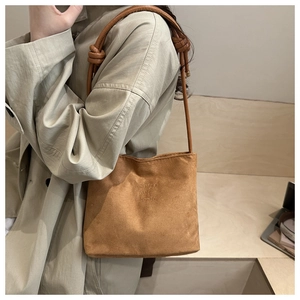 Detail of brown faux suede bucket bag featuring leather shoulder strap with knot detail