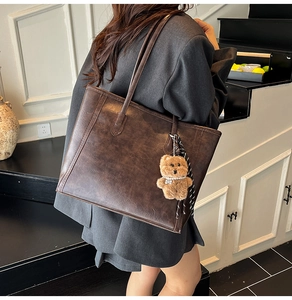 Detail of dark brown leather tote bag with plush bear charm and patterned scarf