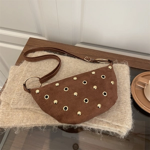 Brown suede crescent bag with gold rivets and adjustable strap on a cozy background