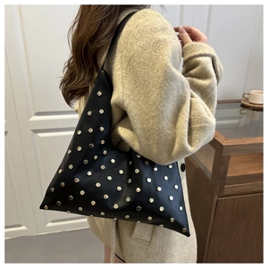 Detail van zwarte matte hobo tas met zilveren klinknagels over de schouder gedragen