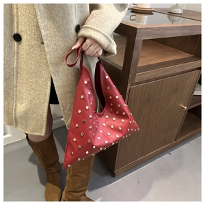 Detail van rode driehoekige lederen tas met gouden studs op een beige jas achtergrond