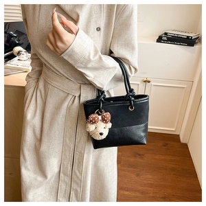 Detail of black mixed-material bucket bag with knotted handles and a plush bear charm